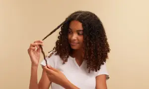 Chica con cabello rizado oscuro, aplicando el método curly a un mechón.