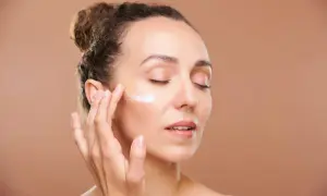 Mujer aplicándose crema en la mejilla, cuidando su piel con retinol en verano.