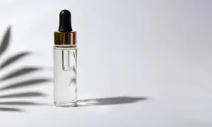 Frasco de vidrio con gotero, contiene un suero transparente, posiblemente con ácido ferúlico, sobre fondo blanco con sombras de hojas.