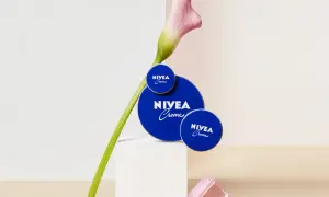Tres latas de crema Nivea azul, con una flor rosa y verde, sobre un pedestal blanco.