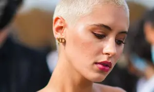 Mujer con atrevidos rapado cortes de pelo corto, luce un maquillaje audaz y pendientes dorados.