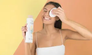 Mujer sonriente con agua micelar y disco desmaquillante, parte de su rutina limpieza facial.