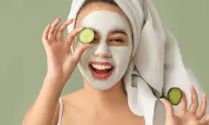 Mujer sonriente con mascarilla facial y rodajas de pepino, disfrutando de tratamientos faciales naturales.