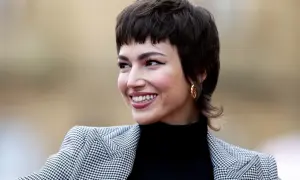 Mujer sonríe con un corte pixie medio, luciendo un blazer de pata de gallo y un pendiente dorado.