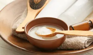 Un tazón con agua de arroz para la cara, una cuchara de madera con arroz, un cepillo para el cabello y botellas de productos de belleza.