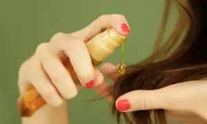 Mano aplica aceite capilar, un producto común en cosmética por sus siliconas, para dar brillo y suavidad al cabello.