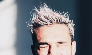 Hombre con pelo rubio despeinado y ojos cerrados. Consejos sobre como hidratar el pelo hombre para un look fresco.