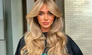 Mujer con cabello rubio largo y ondulado, con un flequillo mariposa que enmarca su rostro.