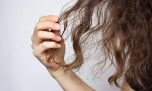 Mano sujetando mechones de cabello castaño, mostrando la necesidad de una repolarización capilar para revitalizarlo.