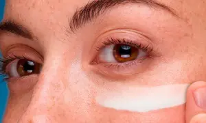 Dedo aplica crema contorno de ojos en toda la cara, cubriendo pecas y piel.