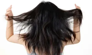 Mujer con cabello oscuro y largo, moviéndolo con las manos. Busca un alisado natural para domar su melena.