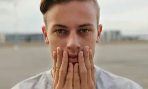 Primer plano de un joven con las manos en la cara, su peinado degradado resalta sus ojos verdes.