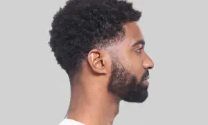 Perfil de hombre con cabello rizado y barba, luciendo un moderno corte taper fade.