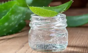Un trozo de hoja de aloe vera descansa sobre un frasco de vidrio con gel transparente, ideal para un tratamiento de aloe vera para el cabello sin enjuagar.