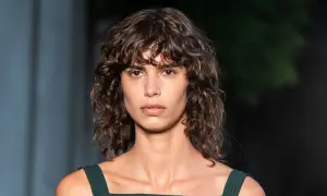 Modelo con un moderno corte de pelo rizado a capas, con mechones que enmarcan su rostro.