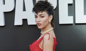 Mujer con un atrevido corte mullet y maquillaje dramático, luciendo un vestido rojo y un collar de perlas.