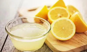 Un tazón de jugo de limón fresco y limones cortados, ideales como remedios caseros para el pelo graso.