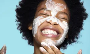 Una mujer sonríe con una mascarilla blanca en la cara. ¿Qué va primero el exfoliante o el limpiador?