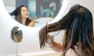 Mujer revisando su cabello graso frente a un espejo, buscando remedios caseros para el cabello graso.