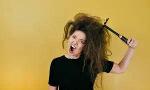 Mujer frustrada con su pelo seco y encrespado, intentando peinarlo con un cepillo.