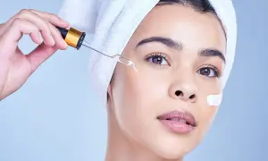 Una mujer con toalla en la cabeza aplica un suero con gotero, ideal para usar niacinamida y retinol juntos.