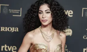 Mujer con cabello oscuro y rizos definidos, luciendo un vestido dorado y un collar de cadenas.