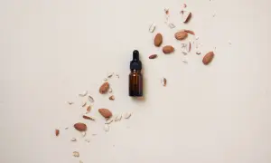 Frasco de aceite de almendras para el pelo rodeado de almendras enteras y trozos.