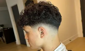 Joven con cabello rizado oscuro y un corte moderno con **low fade** impecable, creando un degradado suave y estilizado en los laterales.