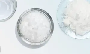 Botes con escamas blancas, como cetearyl alcohol, y un polvo blanco en un plato de vidrio.