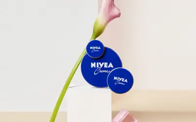 Tres latas de crema Nivea azul, con una flor rosa y verde, sobre un pedestal blanco.