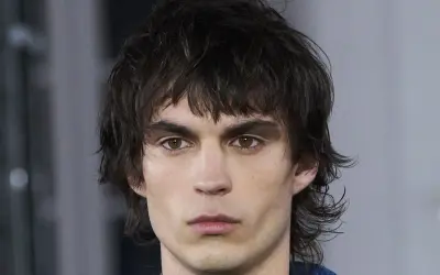 Hombre joven con un moderno mullet corto, cabello oscuro y despeinado, mirada intensa.