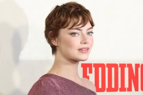 Mujer con pelo corto blanco moderno, ojos azules y vestido rosa brillante.