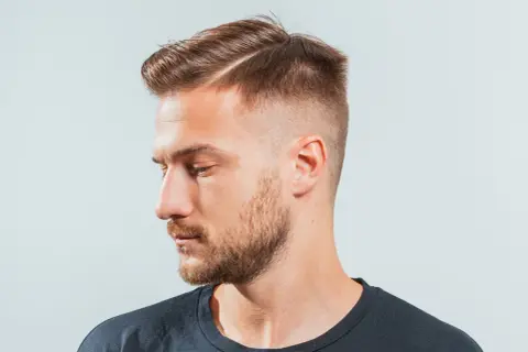 Hombre con un corte de pelo moderno, con un taper fade y raya marcada.