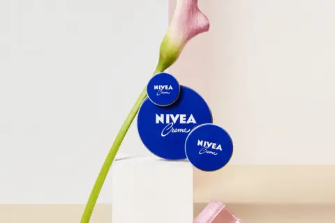 Tres latas de crema Nivea azul, con una flor rosa y verde, sobre un pedestal blanco.