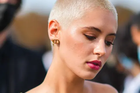 Mujer con atrevidos rapado cortes de pelo corto, luce un maquillaje audaz y pendientes dorados.