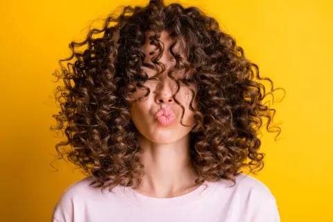 Chica con rizos perfectos, besando al aire. Su cabello luce espectacular gracias al método curlt.