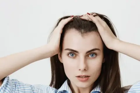 Mujer con las manos en la cabeza, mostrando sus baby hairs y ojos azules intensos.