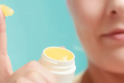 Dedo con vaselina amarilla, mostrando qué es el petrolatum. Un pequeño tarro blanco al lado.