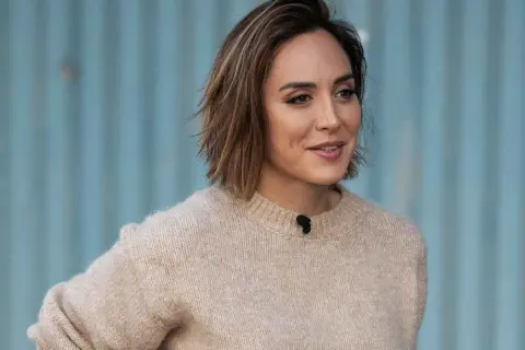 Mujer con un moderno corte bob con flequillo, luciendo un suéter beige y una sonrisa amable.