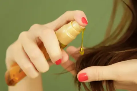Mano aplica aceite capilar, un producto común en cosmética por sus siliconas, para dar brillo y suavidad al cabello.