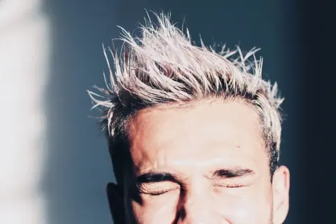 Hombre con pelo rubio despeinado y ojos cerrados. Consejos sobre como hidratar el pelo hombre para un look fresco.