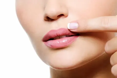 Dedo tocando labios rosados, notando pequeños granitos en los labios.