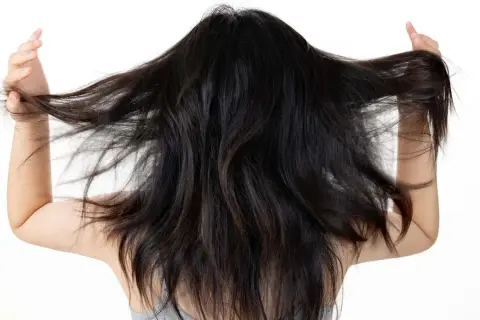 Mujer con cabello oscuro y largo, moviéndolo con las manos. Busca un alisado natural para domar su melena.