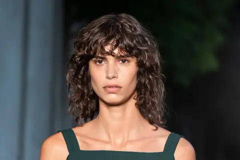 Modelo con un moderno corte de pelo rizado a capas, con mechones que enmarcan su rostro.