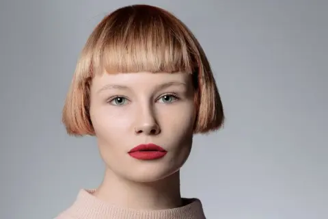 Mujer con pelo corto con flequillo desfilado, ojos azules y labios rojos.