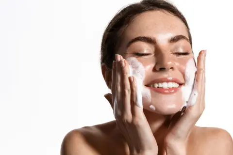 Una mujer sonríe mientras se realiza una limpieza facial noche con espuma.
