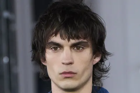 Hombre joven con un moderno mullet corto, cabello oscuro y despeinado, mirada intensa.