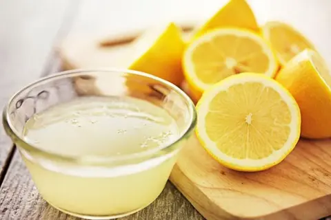 Un tazón de jugo de limón fresco y limones cortados, ideales como remedios caseros para el pelo graso.