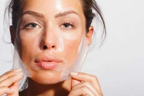 Mujer retirando una mascarilla de su rostro, un paso clave para como alisar la piel de la cara y lograr un cutis radiante.