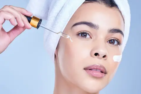 Una mujer con toalla en la cabeza aplica un suero con gotero, ideal para usar niacinamida y retinol juntos.